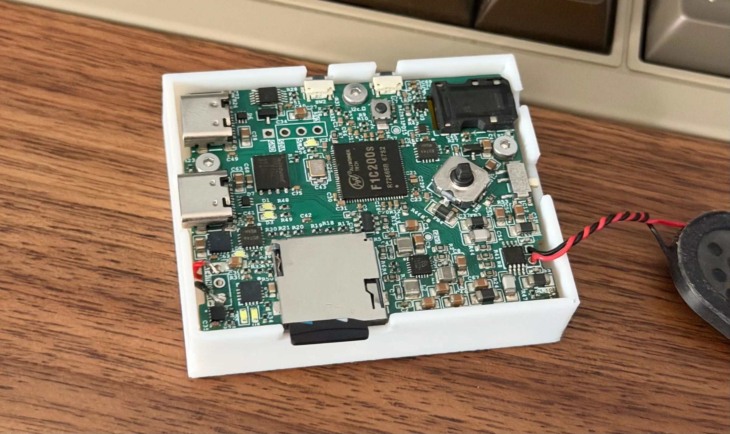 The finished MP3 player board in its white 3D printed case, on a desk next to a keyboard